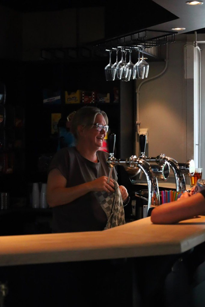 Gastvrouw glimlachend achter de bar bij Plek lunchroom